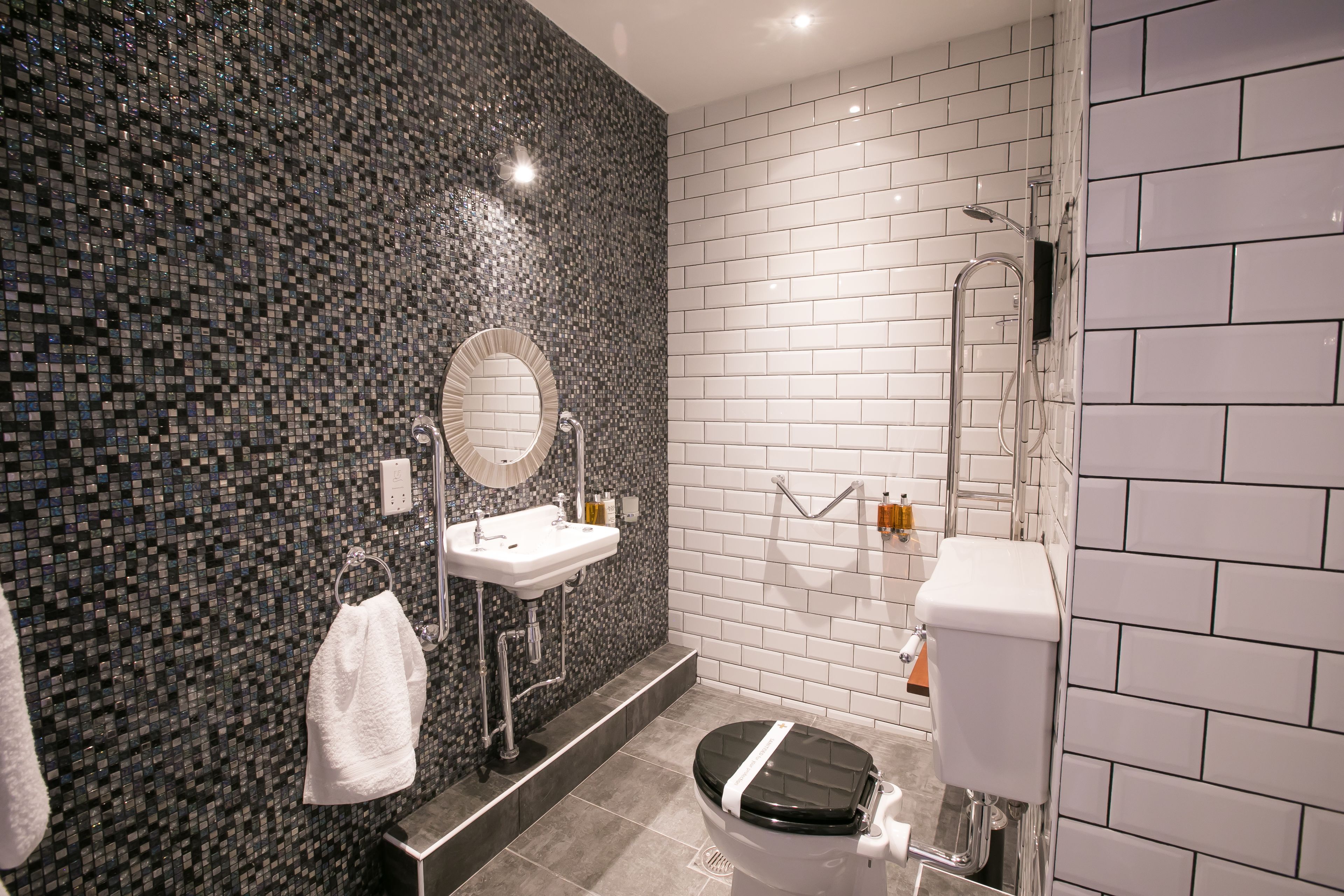 A modern bathroom with a mosaic tile wall, a round mirror, a toilet, and a shower.