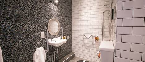 A modern bathroom with a mosaic tile wall, a round mirror, a toilet, and a shower.