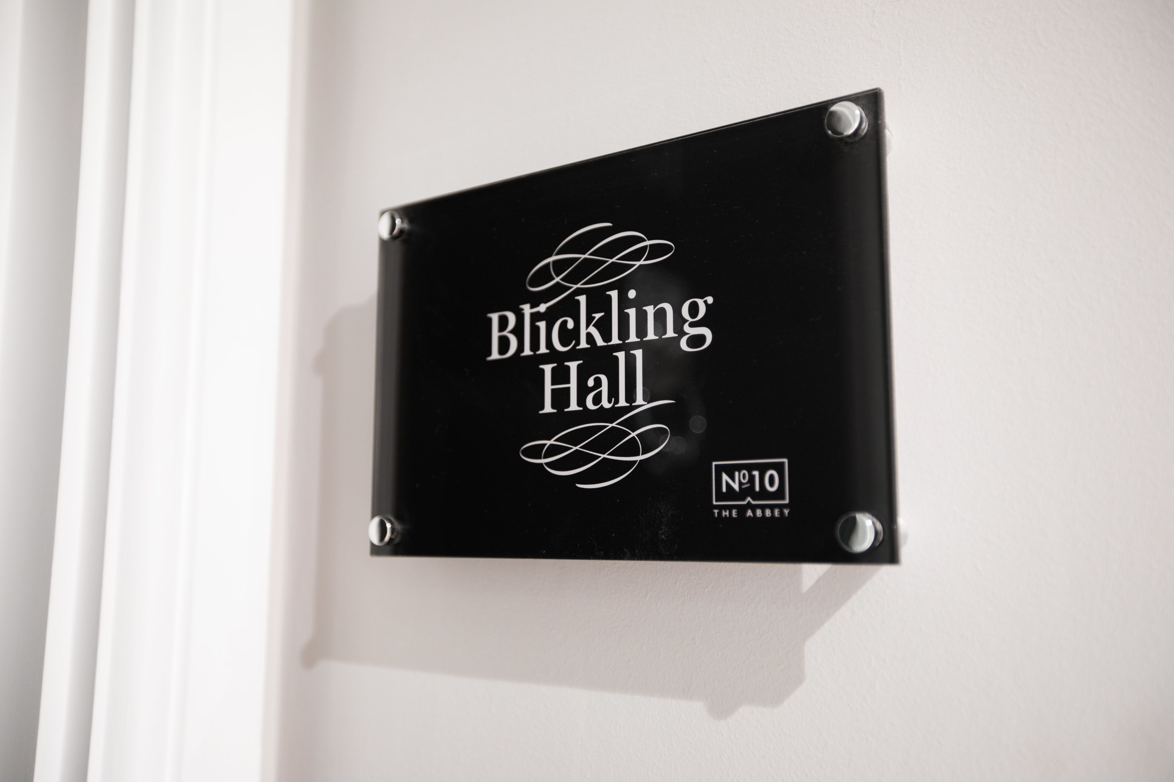 Un cartell negre amb lletres blanques a la paret, que diu 'Blickling Hall' i 'Número 10 The Abbey'.