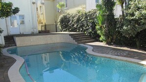 Ein rechteckiger Pool mit einer Fliesenleiste, umgeben von einem befestigten Bereich und Treppen zu einem Gebäudeeingang.