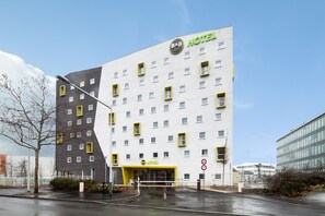 A modern hotel building with a white facade and yellow accents, featuring multiple windows and a prominent 'B&B HOTEL' sign.