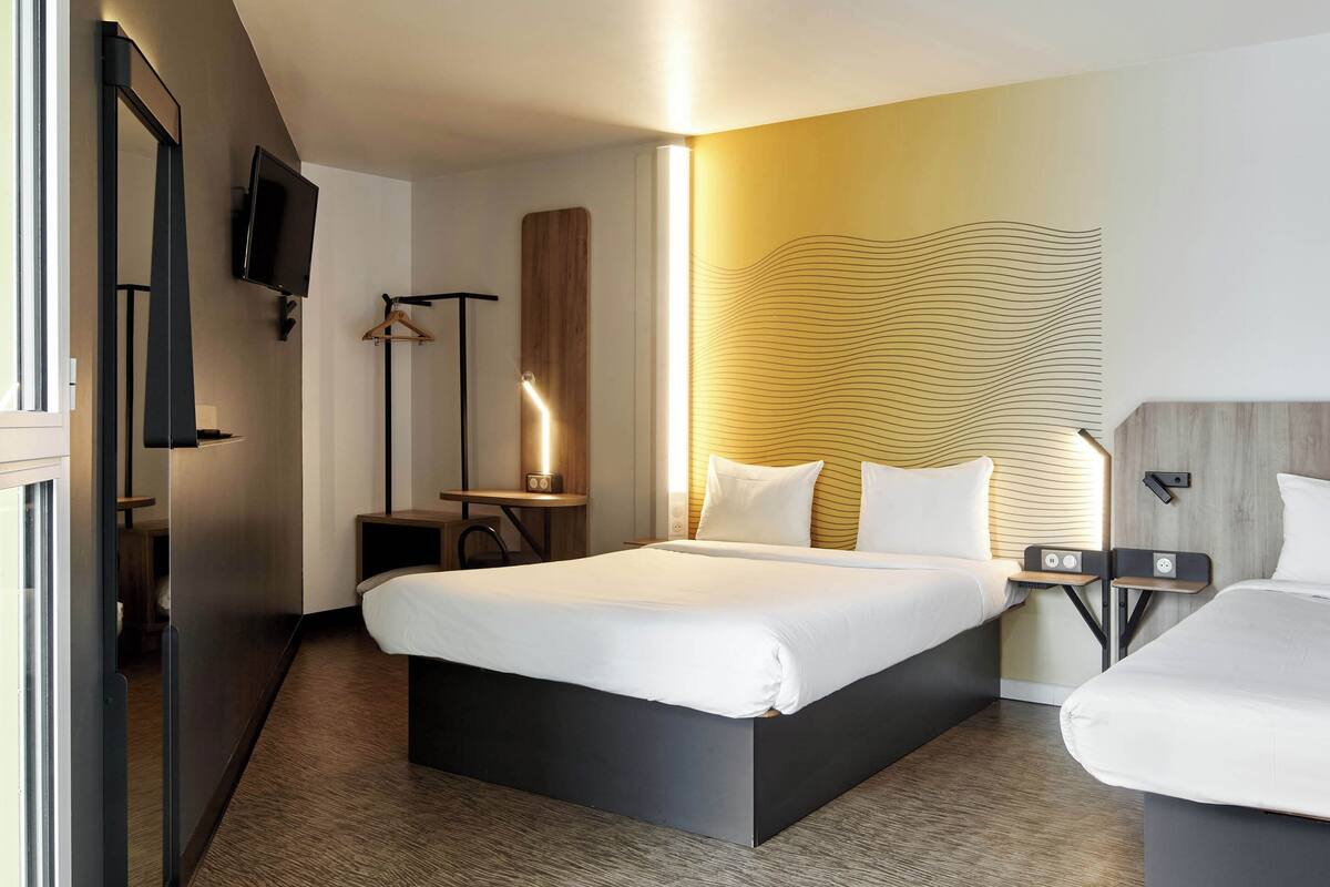 A modern hotel room with a large bed, bedside tables, a TV, and a unique wall design.