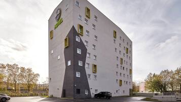Un hôtel moderne au design triangulaire original, doté de nombreuses fenêtres et d’un espace de stationnement situé à l’avant.