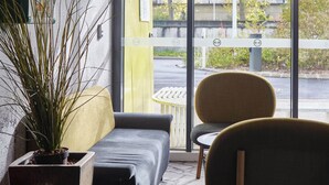 A modern interior with a sofa, a chair, and a potted plant near a window. - B&B HOTEL NANTERRE Rueil Malmaison (Nanterre)