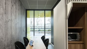 A conference room with a wooden table, black chairs, a glass wall, and a microwave in a wooden cabinet.