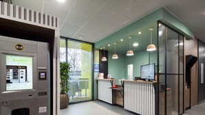 A reception area with a self-service kiosk, a reception desk, pendant lighting, and a large potted plant. - B&B HOTEL NANTERRE Rueil Malmaison (Nanterre)