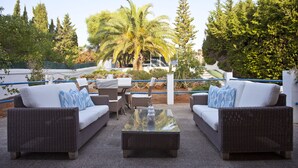 Un área de estar al aire libre con mobiliario de mimbre, una mesa de vidrio y una palmera.