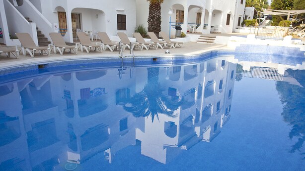 Una piscina azul cristalina con sillas de descanso blancas y una escalera que lleva a una zona cubierta.