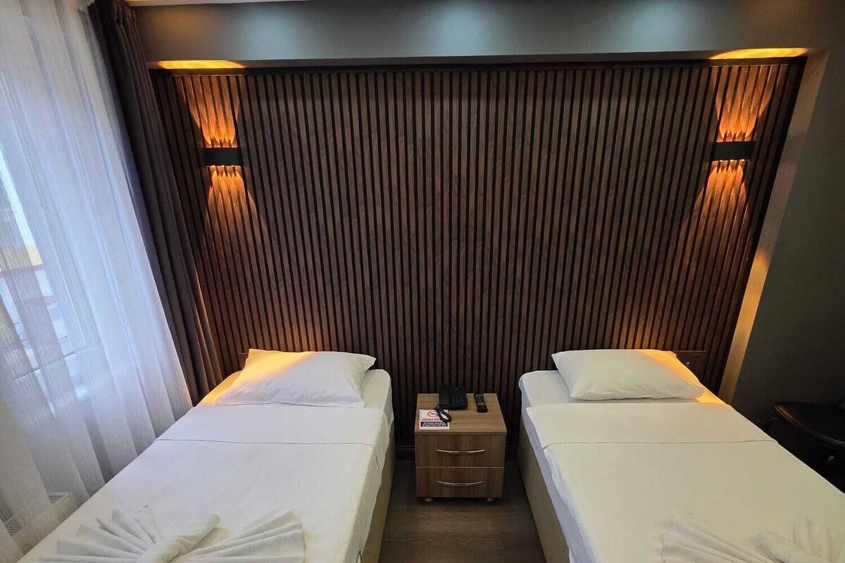 A hotel room with two beds, each with a neatly folded towel and a bedside table with a phone and a sign.