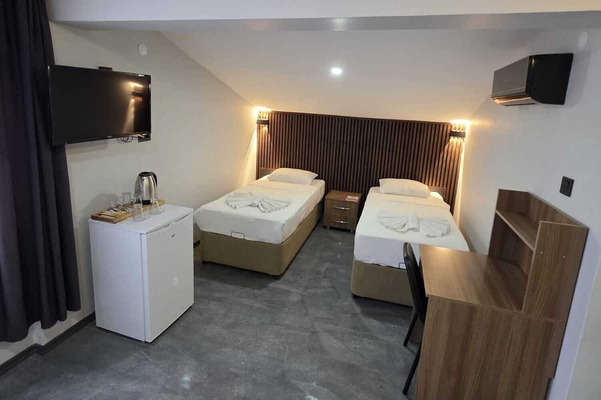A modern hotel room with two beds, a small kitchenette, a flat-screen TV, and a wooden desk.