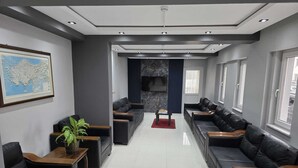 A modern living room with black leather sofas, a coffee table, a potted plant, and a large framed map on the wall. - Gizem Pansiyon (Çanakkale)