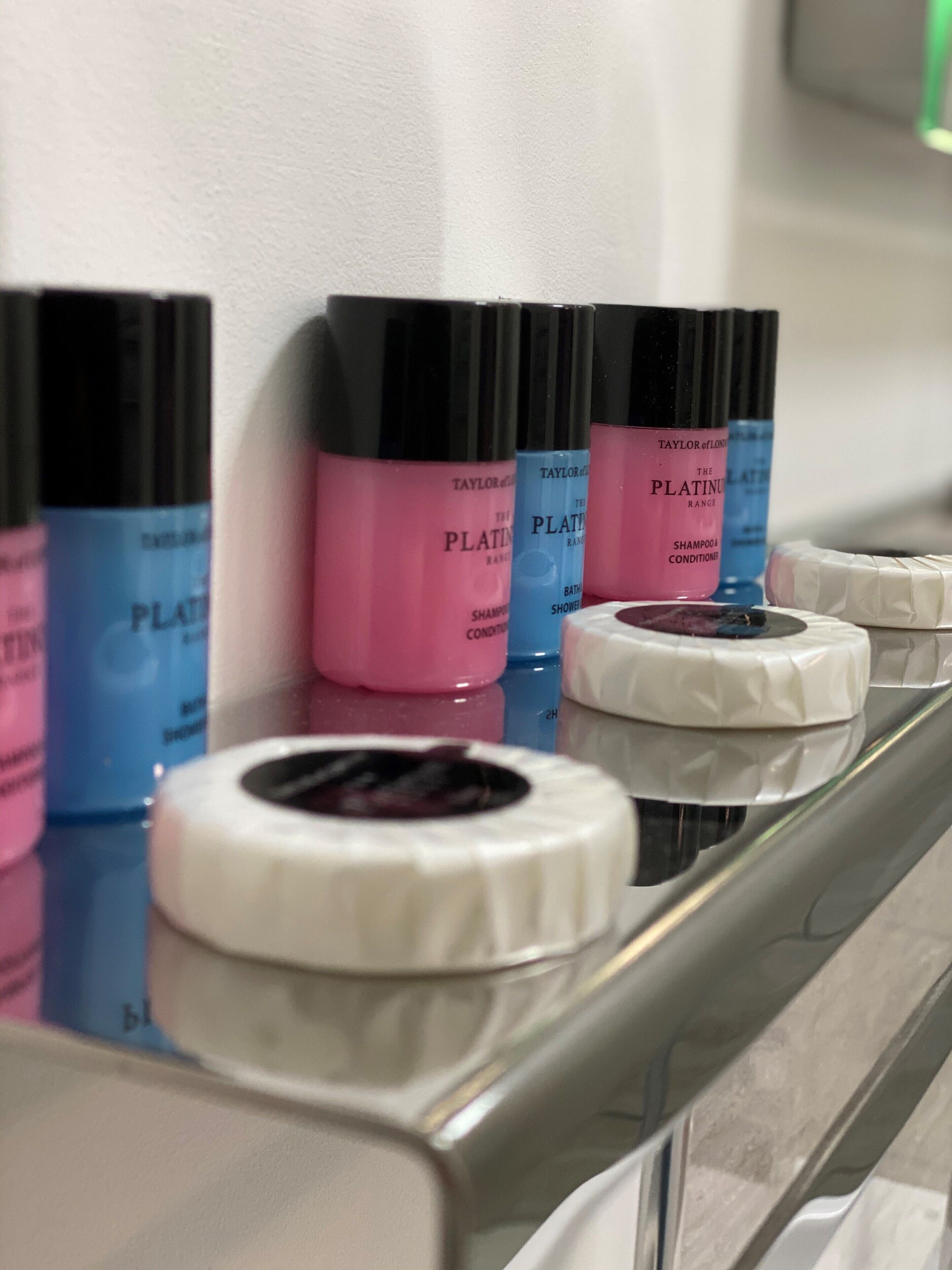 Pesualtaan reunalla on useita pulloja Taylor of Londonin The Platinum Range -sarjan shampoota ja hoitoainetta, valkoinen pyyhe ja rulla valkoista wc-paperia.