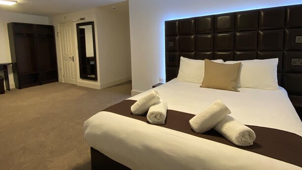 A hotel room with a large bed, a dark headboard, and a flat-screen TV mounted on the wall. - The Charles Hotel (Chatham)