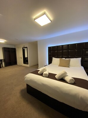Habitación de hotel con una cama grande, cabecera oscura y televisor de pantalla plana montado en la pared.