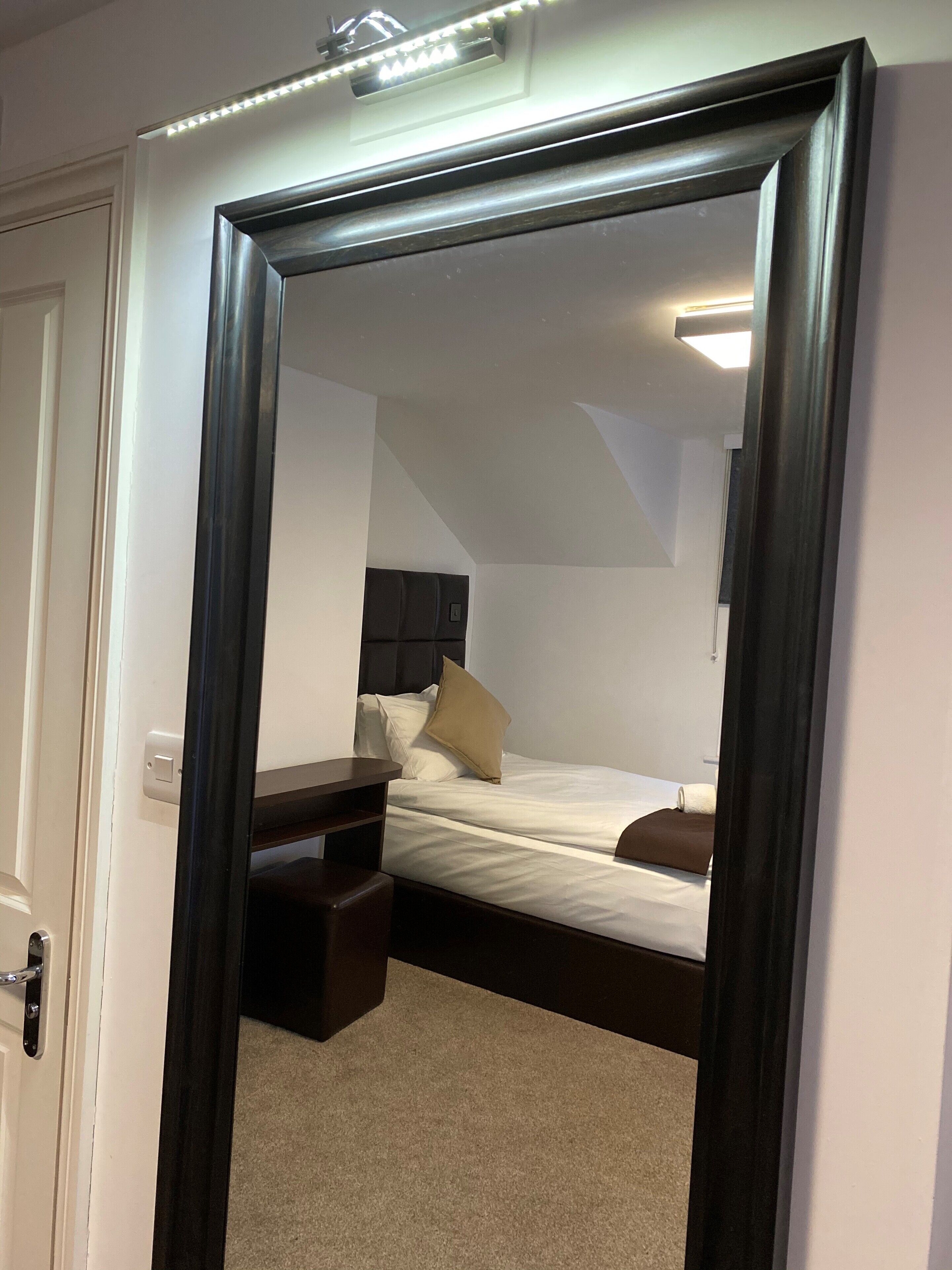 Un dormitorio con cama, mesita de noche y espejo.
