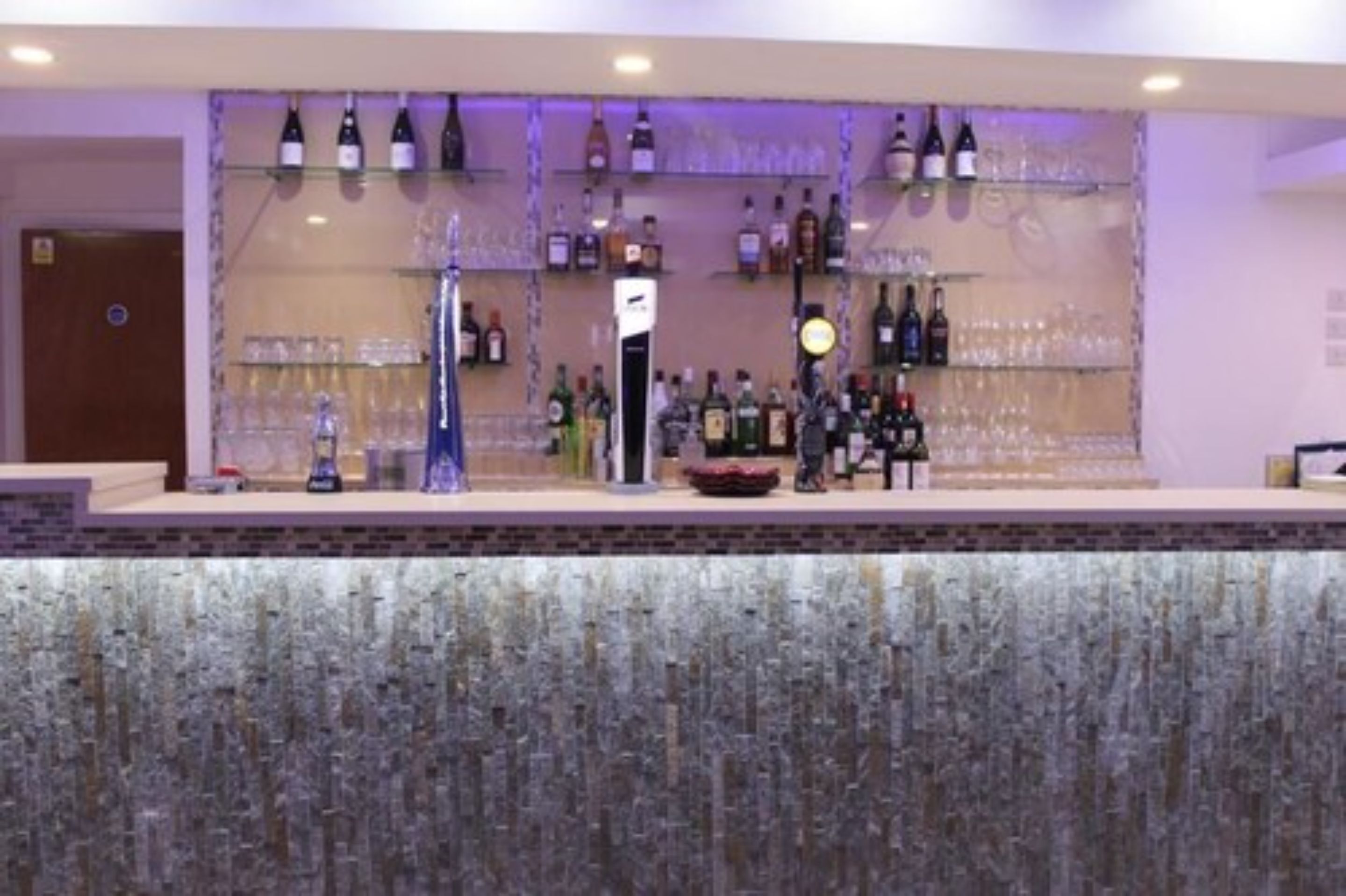 A bar area with shelves of bottles and glasses, a clock, and a decorative vase.
