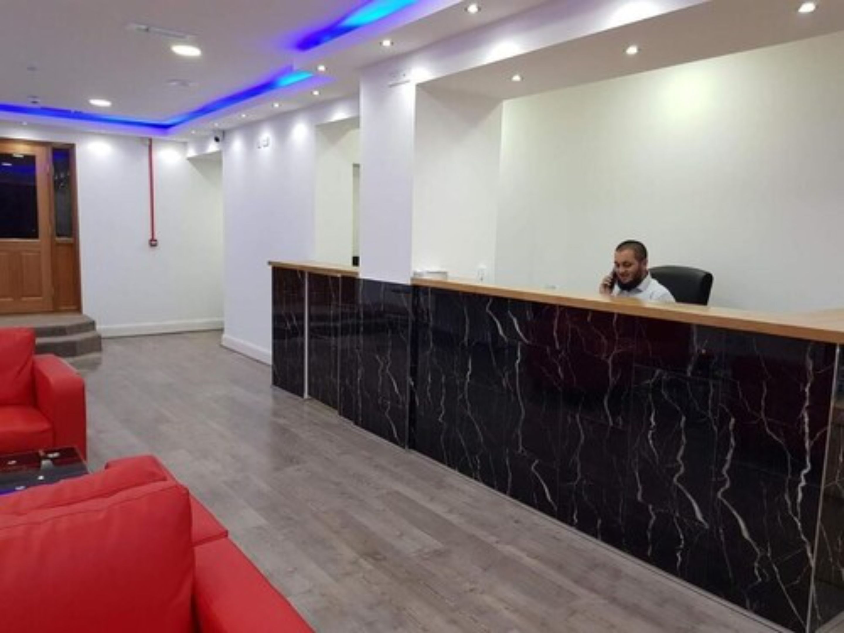 A reception area with a marble counter, red seating, and a modern ceiling design.