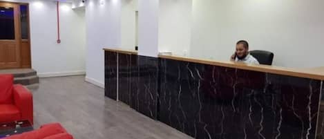 A reception area with a marble counter, red seating, and a modern ceiling design.