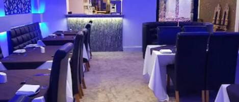 Un restaurante con diseño moderno, que cuenta con una zona de bar, diferentes disposiciones de asientos y una pared decorativa.