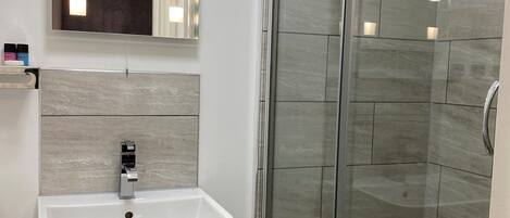 Un baño con ducha de vidrio, lavamanos pedestal y espejo con iluminación.