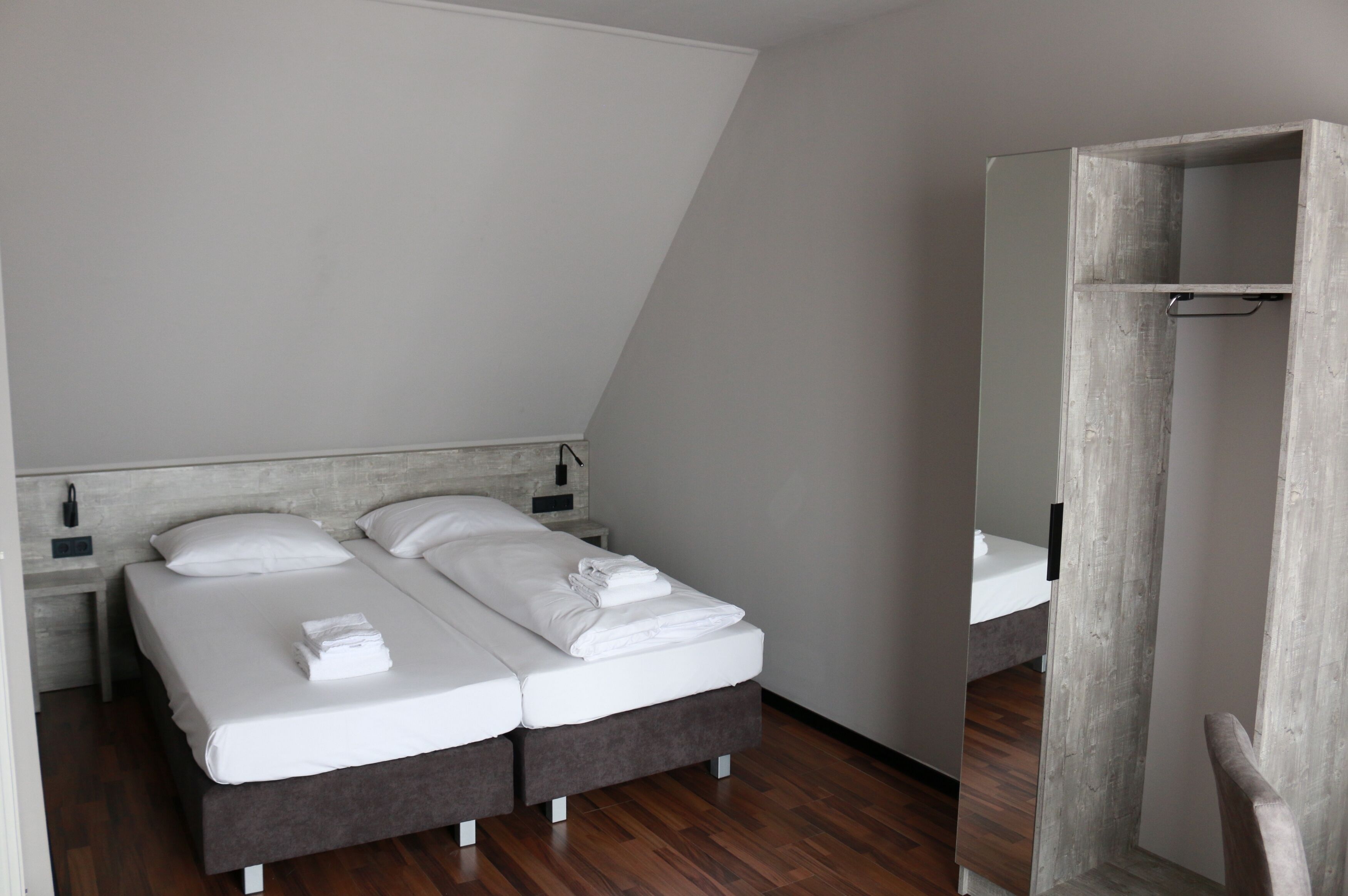 A modern bedroom with two single beds, a wooden floor, and a large mirror.