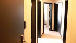 A hallway with multiple doors, a light-colored carpet, and a door handle on the left. - Urban Home Self Check-In Hotel (Hamburg)