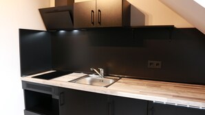 A modern kitchen with black cabinetry, a wooden countertop, and a stainless steel sink. - Urban Home Self Check-In Hotel (Hamburg)