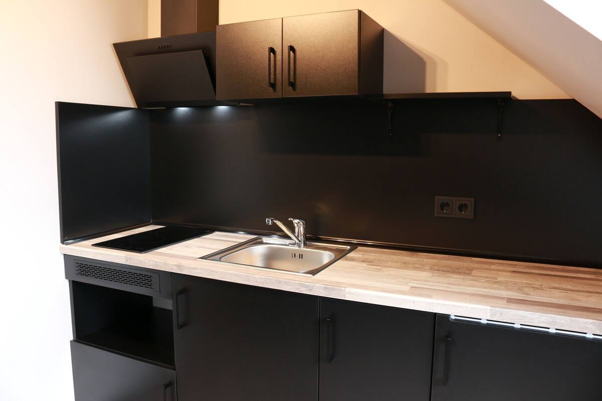 A modern kitchen with black cabinetry, a wooden countertop, and a stainless steel sink.