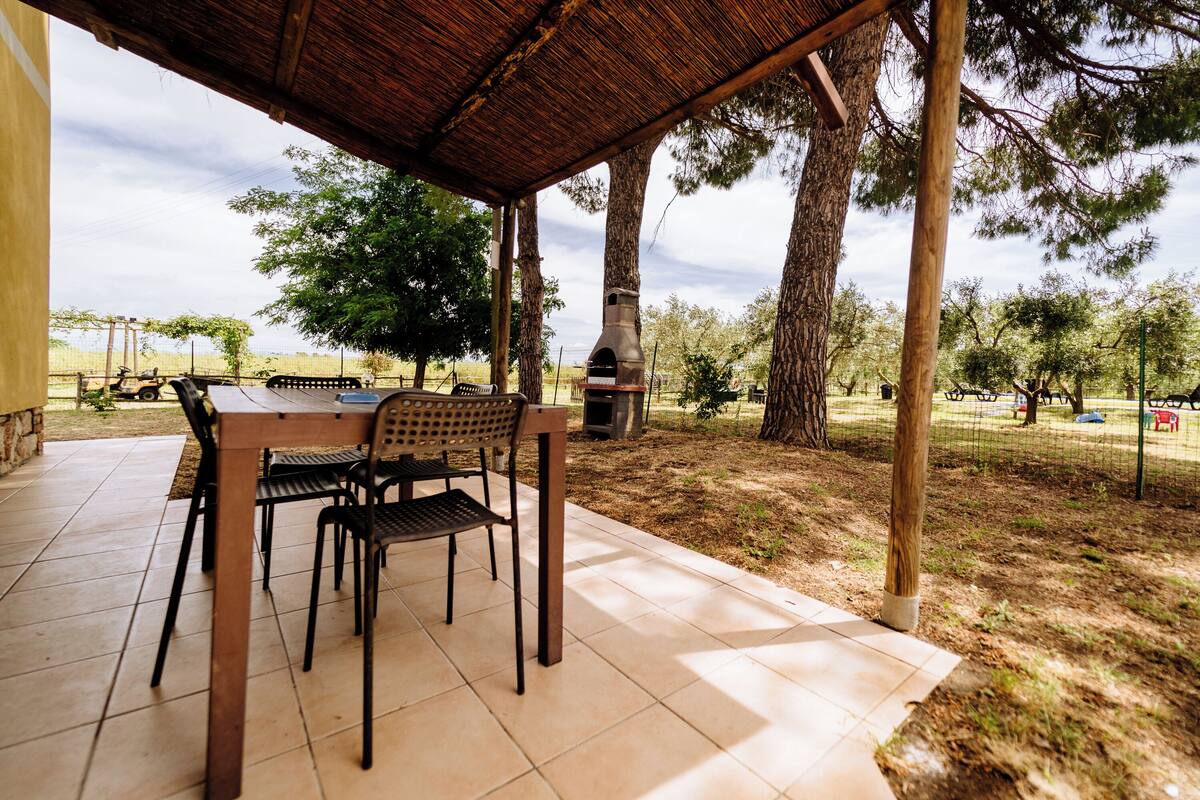 An outdoor patio with a table and chairs, a barbecue grill, and a view of trees and a distant landscape.