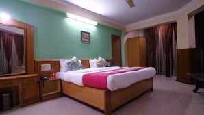 Une chambre d’hôtel avec un lit en bois, une table de chevet, un miroir, une armoire et un ventilateur de plafond.