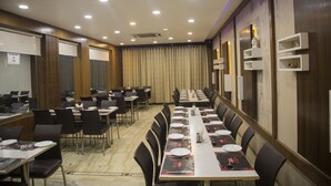 Une salle de conférence avec de longues tables, des chaises noires et un rideau en fond.