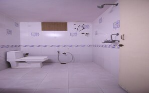 Une petite salle de bain blanche, équipée de toilettes, d’une douche et d’un lavabo.