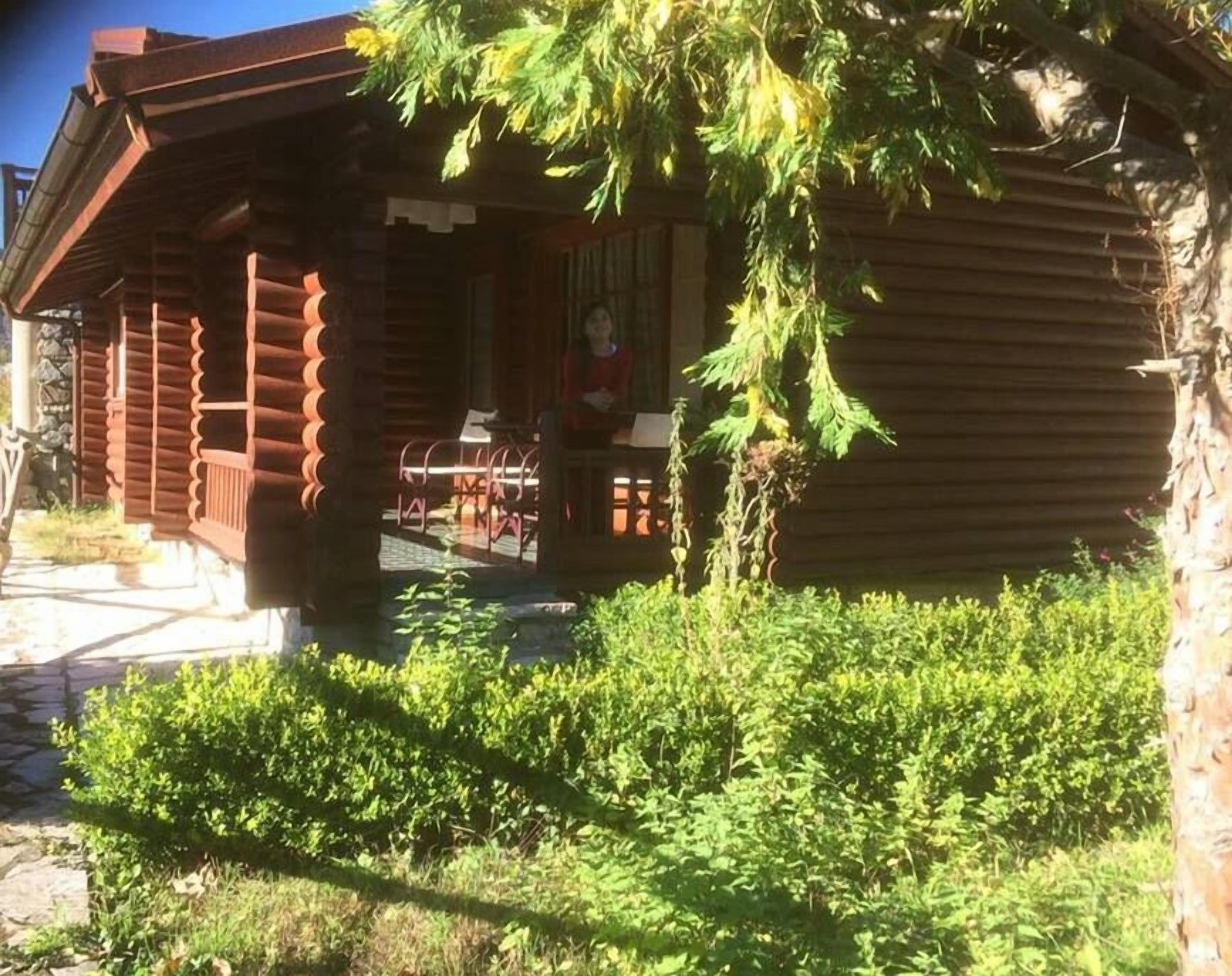 Una cabaña de madera con un porche, una zona de comedor y un pequeño jardín.
