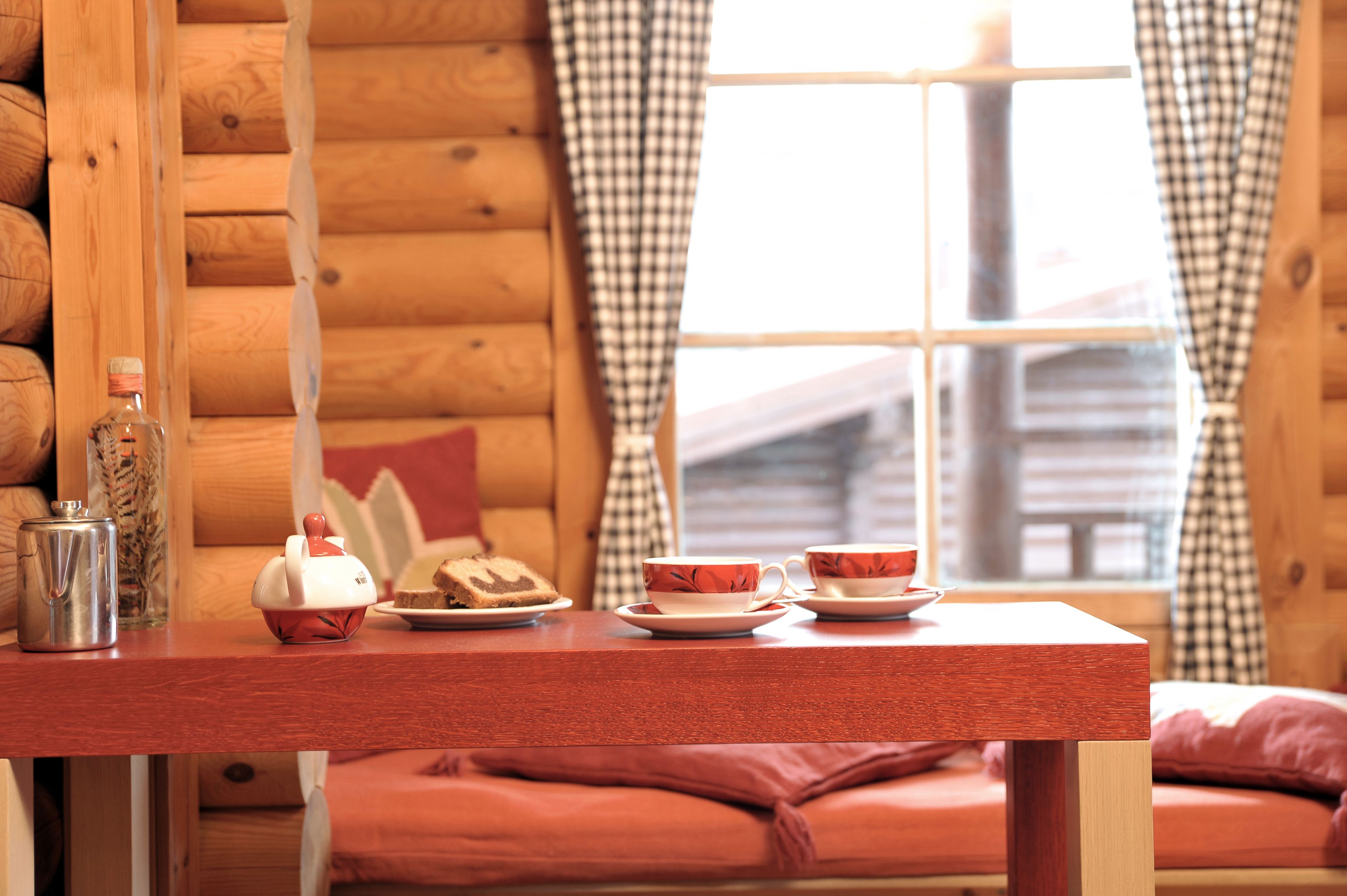 A wooden cabin interior with a wooden table set for tea, a bottle, and a teapot.