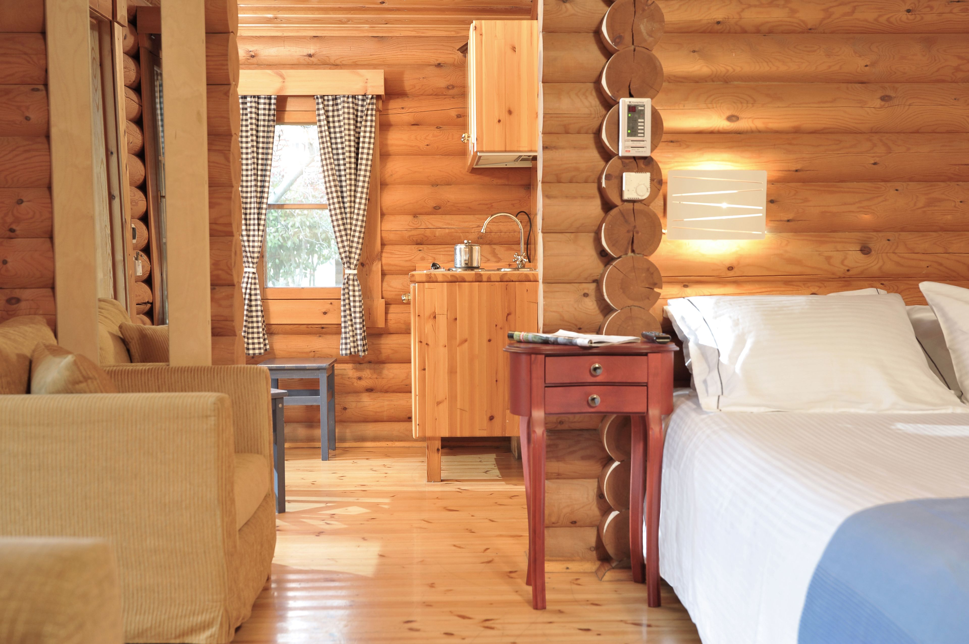 A cozy log cabin room with a bed, a small table, a chair, a wooden cabinet, and a window with curtains.