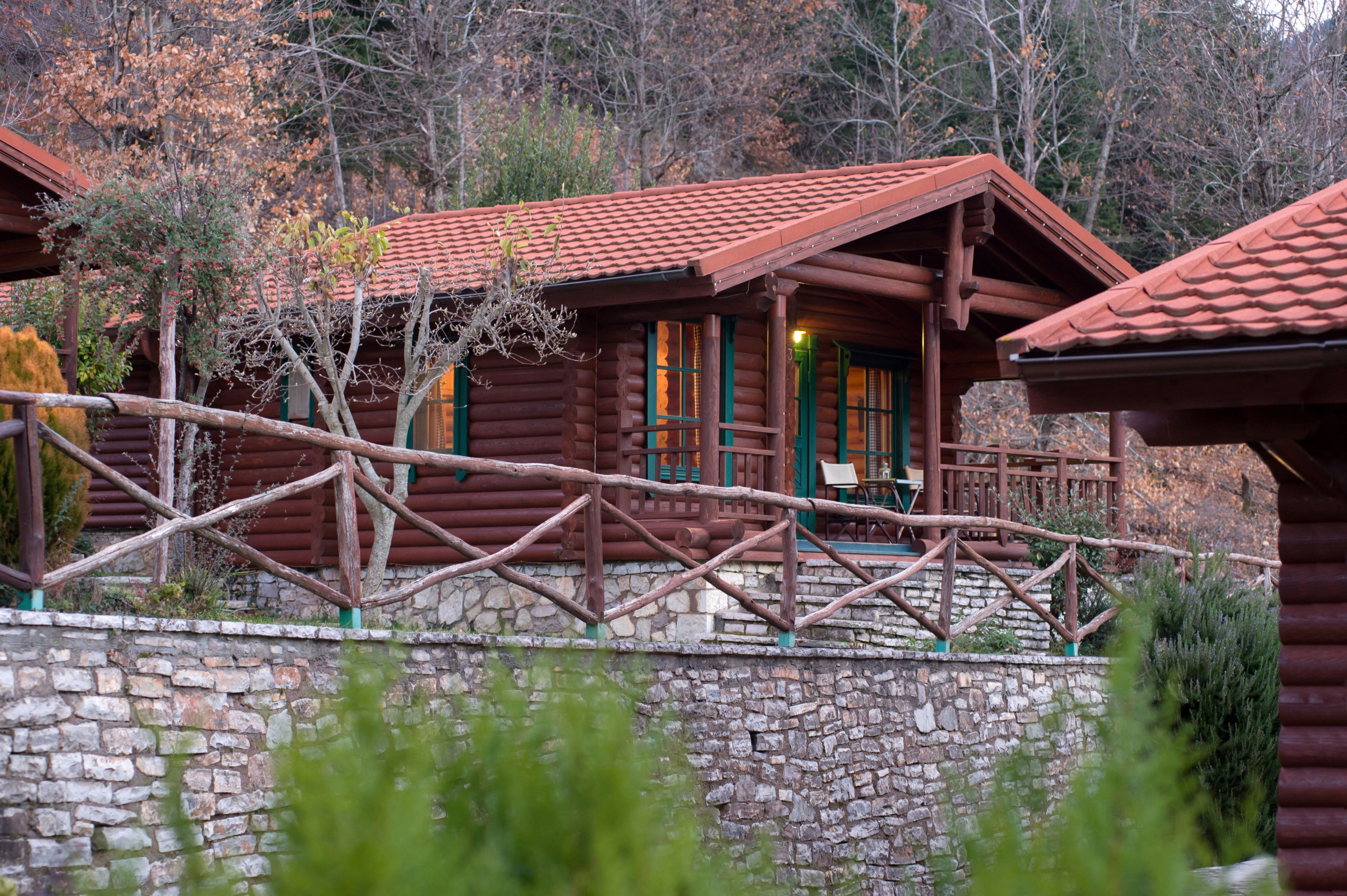 Una cabaña rústica de troncos con cimientos de piedra, terraza de madera y cerca de madera.