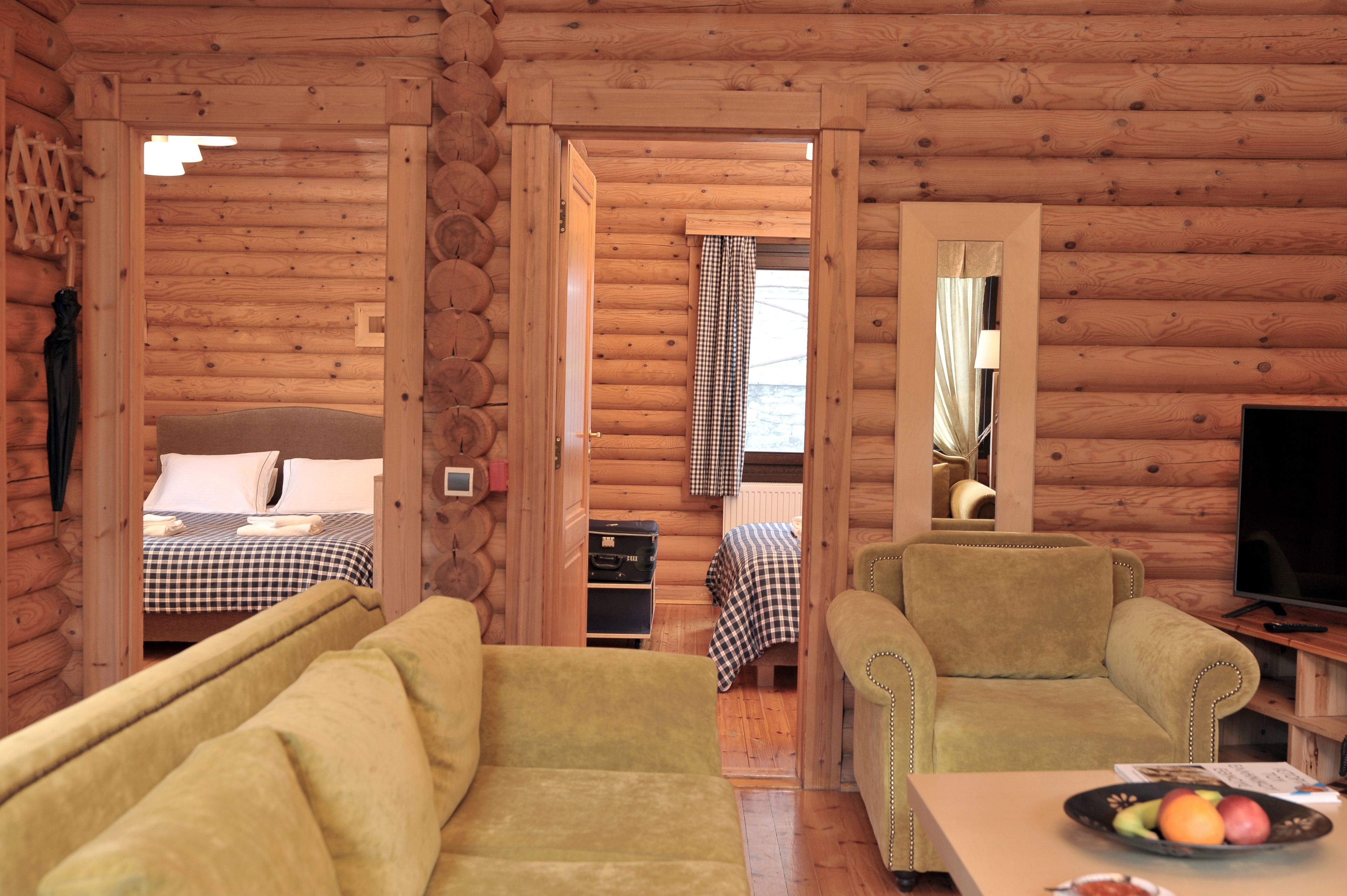 A cozy log cabin room with a sofa, a small table with fruit, a television, and a bed with checkered bedding.