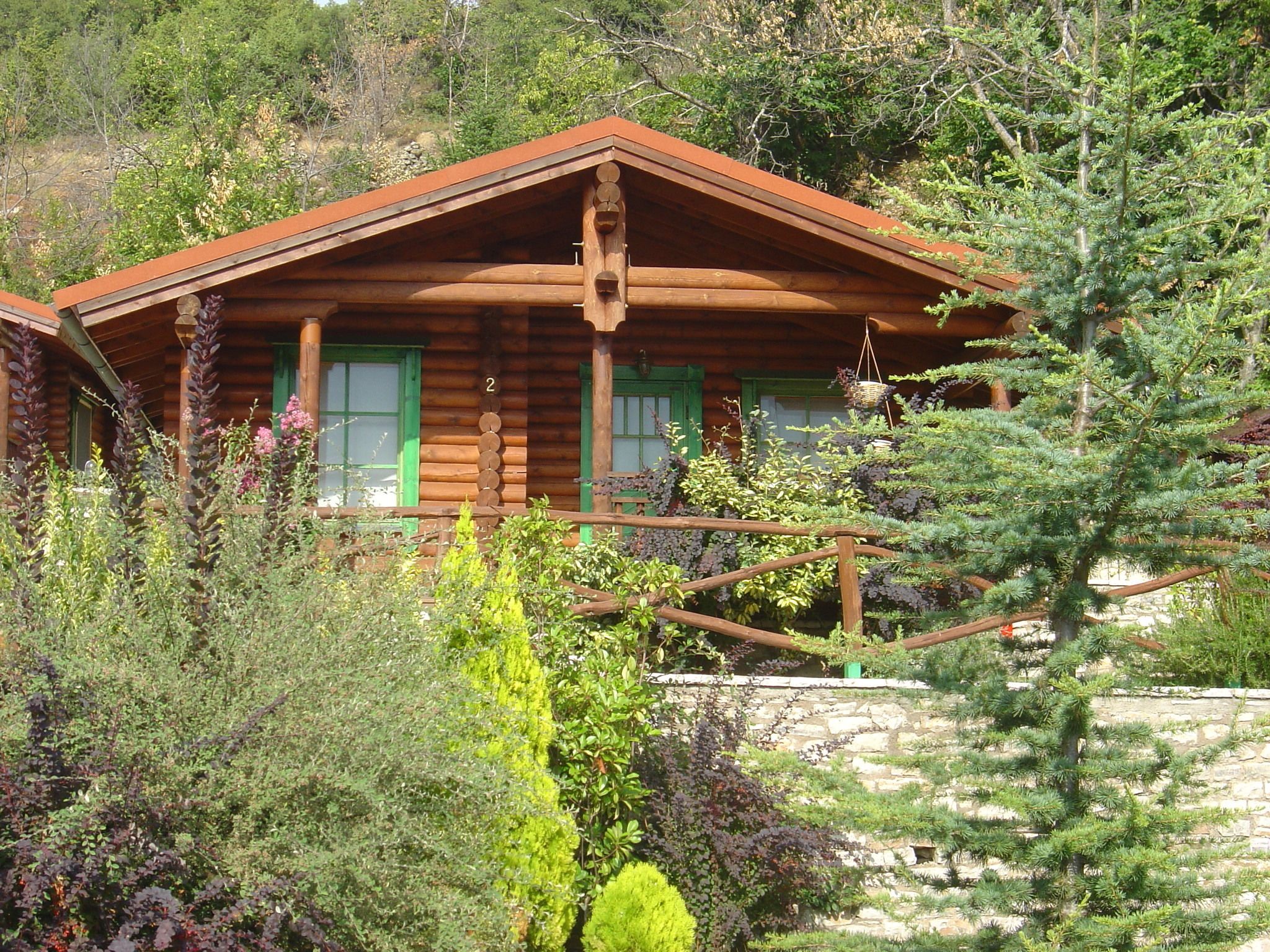 A rustic log cabin with a wooden porch, green shutters, and a stone foundation.