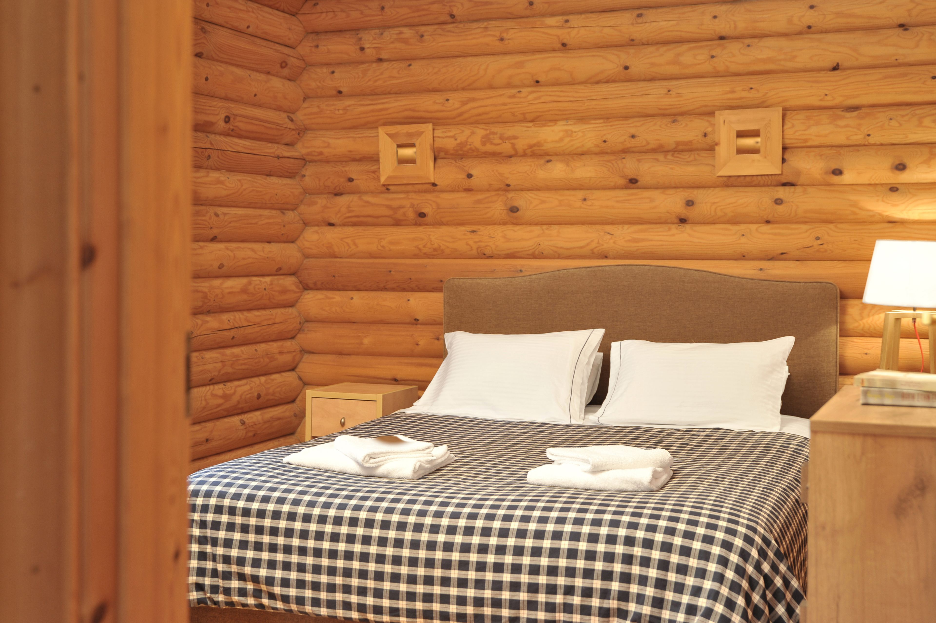 A wooden cabin-style room with a checkered bedspread, two pillows, and neatly folded towels on the bed.