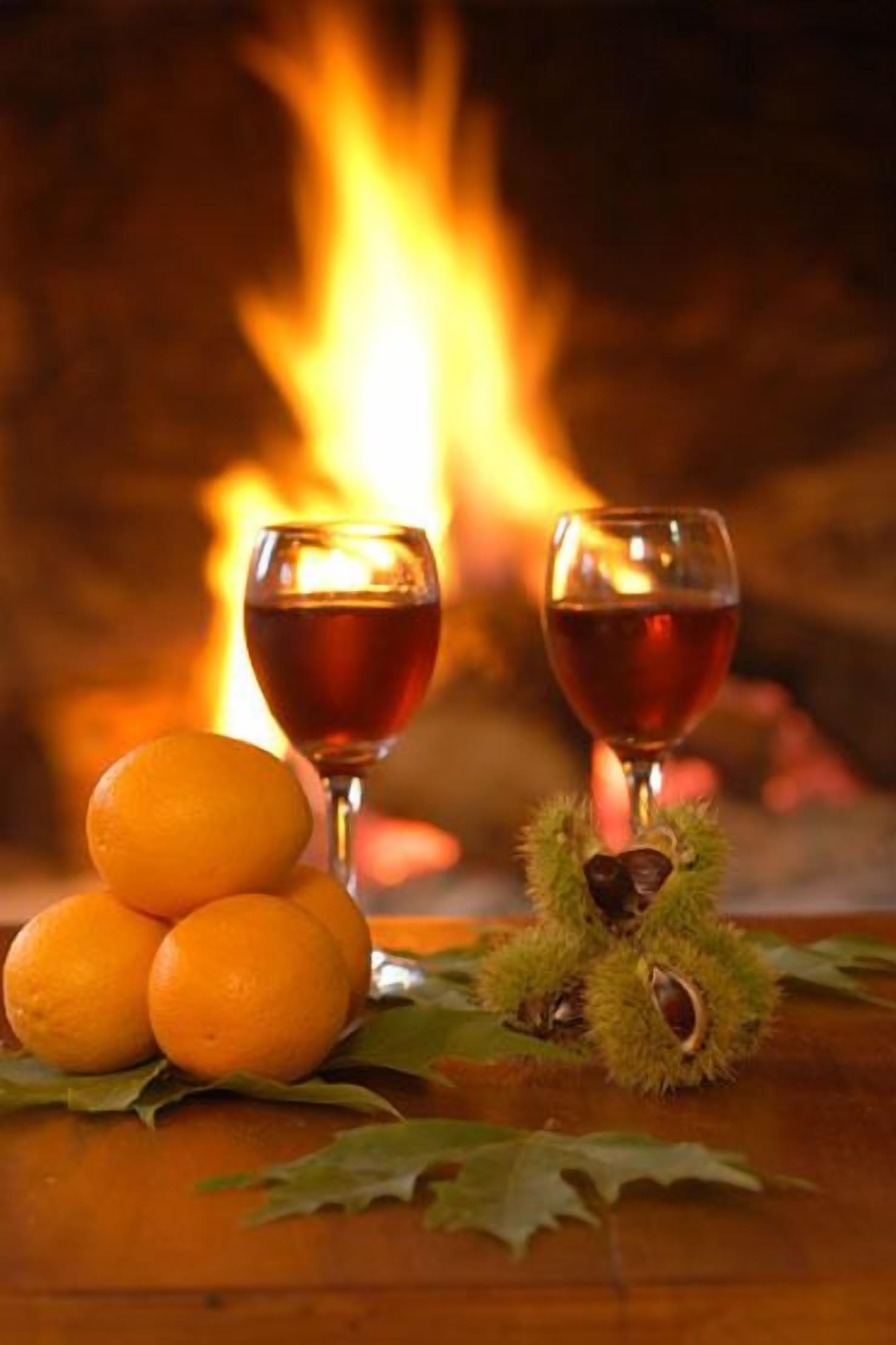 A fireplace with two glasses of red wine and oranges on a table.