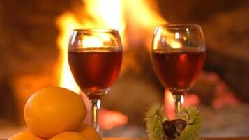 A fireplace with two glasses of red wine and oranges on a table.