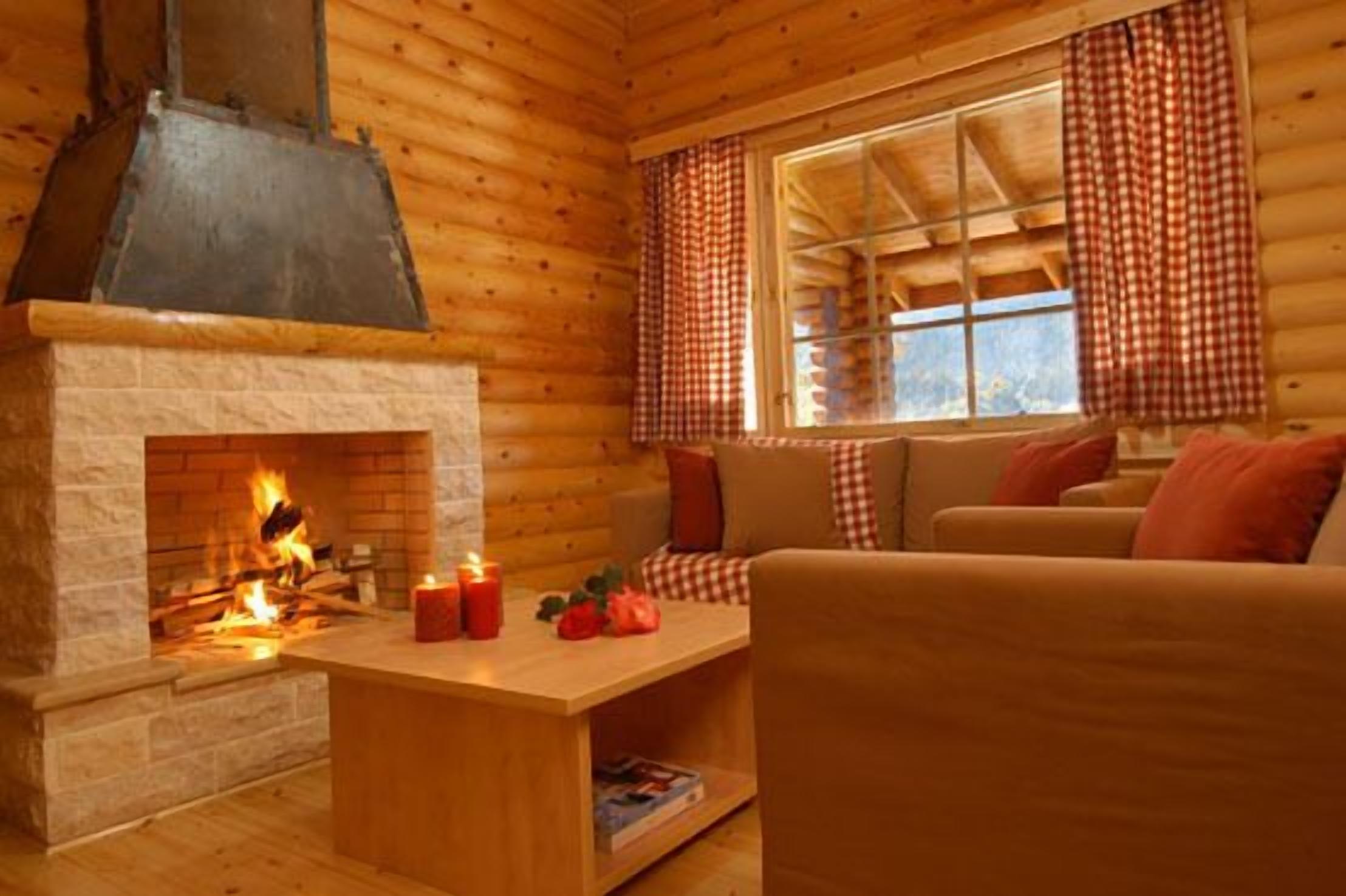 A cozy cabin interior with a fireplace, wooden walls, a sofa, and a window with checkered curtains.