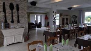 Un restaurante con varias mesas dispuestas para comensales, un mostrador blanco con una carta y un interior acogedor con pared de piedra y mobiliario de madera.