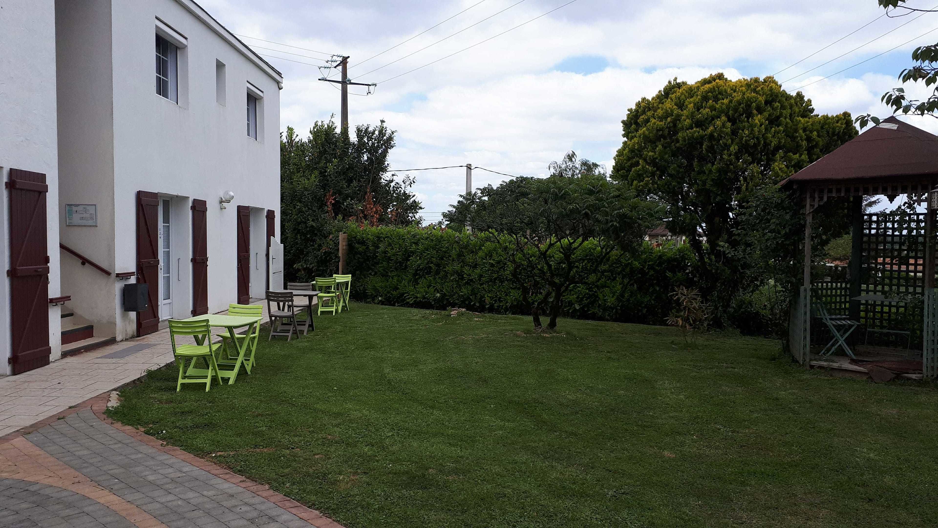 A white building with a covered outdoor seating area, a small garden, and a gazebo.
