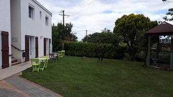 A white building with a covered outdoor seating area, a small garden, and a gazebo.
