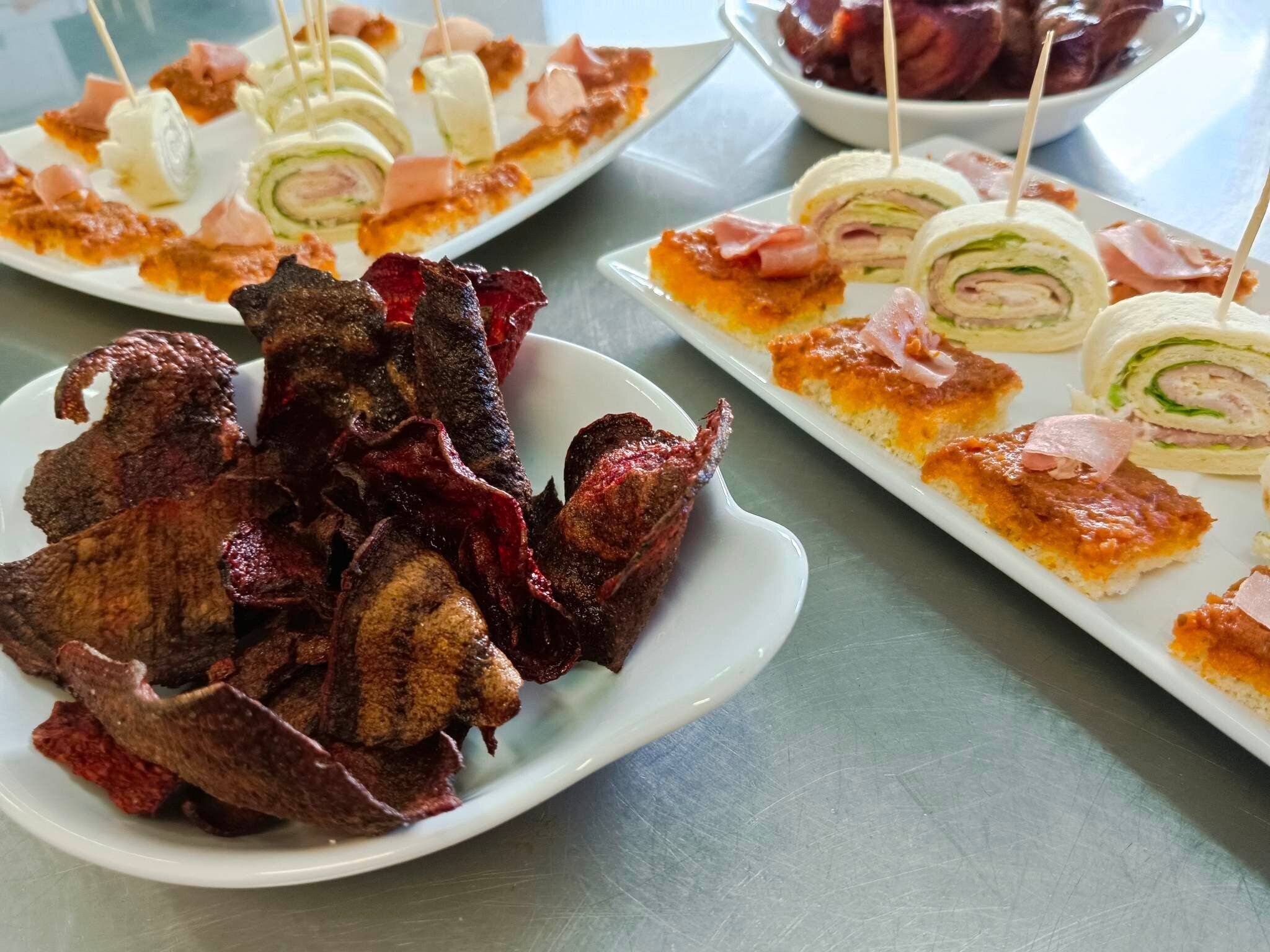 A variety of appetizers including skewered meats, rolled sandwiches, and small bites on white plates.