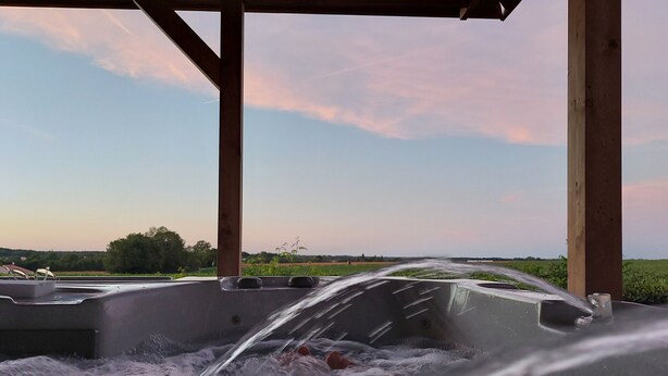 Un jacuzzi con agua saliendo, ubicado debajo de una estructura de madera y con vista a un campo y al cielo.