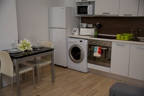 A compact kitchen with a washing machine, microwave, and a small dining area with a table and chairs.