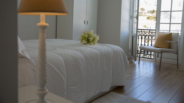 A bedroom with a bed, a white lamp, a bench, and a view of the outside through a window. - Azores Horta Apartments (Horta)