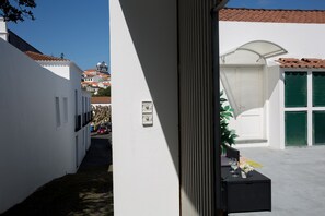 Une ruelle étroite, avec un bâtiment blanc sur la gauche et un bâtiment blanc aux volets verts sur la droite.